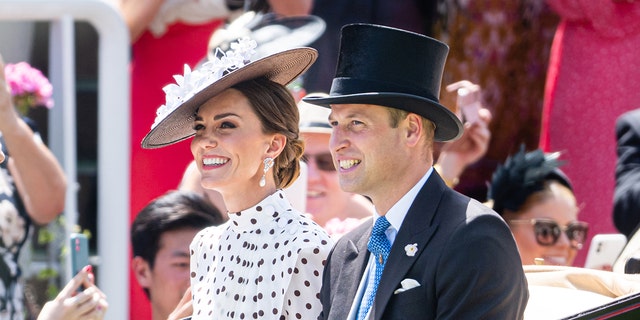 Kate Middleton in a black and white polka dress sitting next to Prince William in a suit and top hat