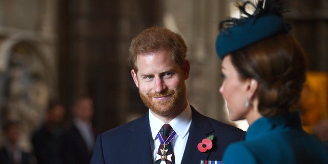 Prince Harry in a suit and tie admiring Kate Middleton in a blue dress with a matching fascinator