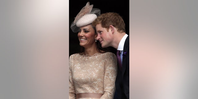 Kate Middleton in a pink dress and matching hat and Prince Harry leans closer to her