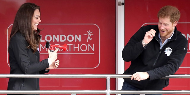 Kate Middleton laughing and blowing a horn in front of a startled Prince Harry