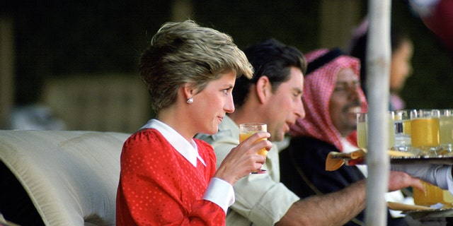 Princess Diana wearing a red and white dress drinking next to Prince Charles