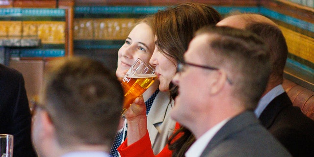 Kate Middleton wearing a red dress drinking a beer