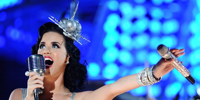 A close-up of Katy Perry wearing a silver fascinator and singing to a mic wearing a silver strapless dress