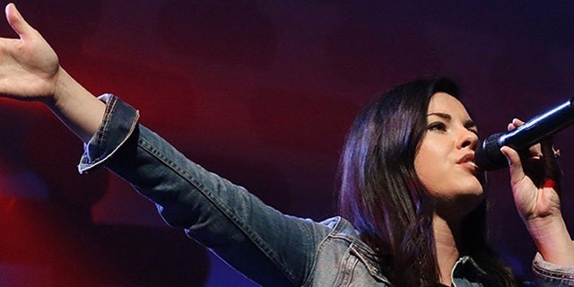 A close-up of Tasha Layton wearing a denim jacket and singing to a mic.