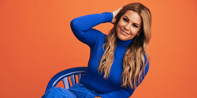 Tasha Layton wearing a cobalt blue turtleneck sweater and matching pants sitting on a blue chair