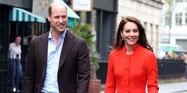 Prince William smiles as he walks alongside Kate Middleton in a red dress