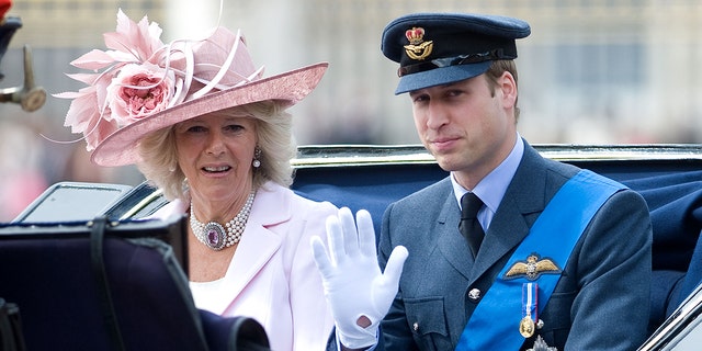 Prince William in a military suit sitting next to Queen Camilla in a pink dress and matching hat