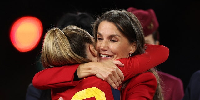 Queen Letizia hugging a football player wearing a red blazer