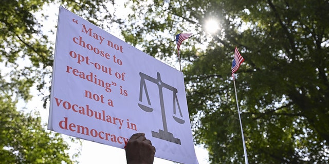 A protest sign reads, "'May not choose to opt-out of reading' is not a vocabulary in democracy"