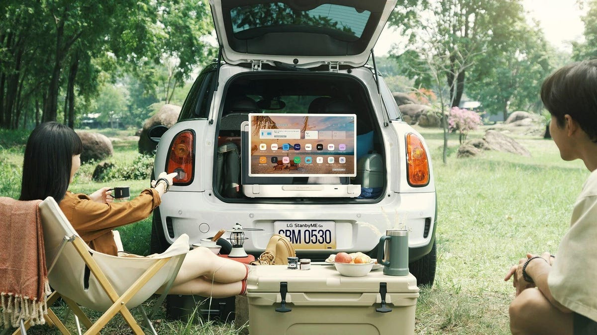 a couple in camping chairs watch the LG StanbyMe Go TV in the back of a car