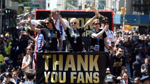 USA women's soccer team midfielder Megan Rapinoe (C) holds up the World Cup 2015 trophy as midfielder Carli Lloyd (2nd L), New York City Mayor Bill de Blasio and head coach Jill Ellis (R) wave to the crowd during the ticker tape parade in New York on July 10, 2015. AFP PHOTO/JEWEL SAMAD        (Photo credit should read JEWEL SAMAD/AFP via Getty Images)