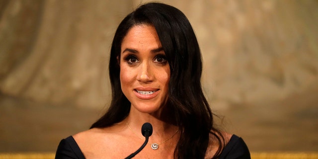 A close-up of Meghan Markle wearing a black dress speaking to the podium