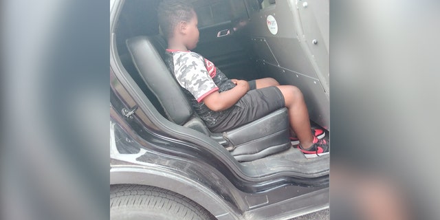Boy shown in back of squad car.