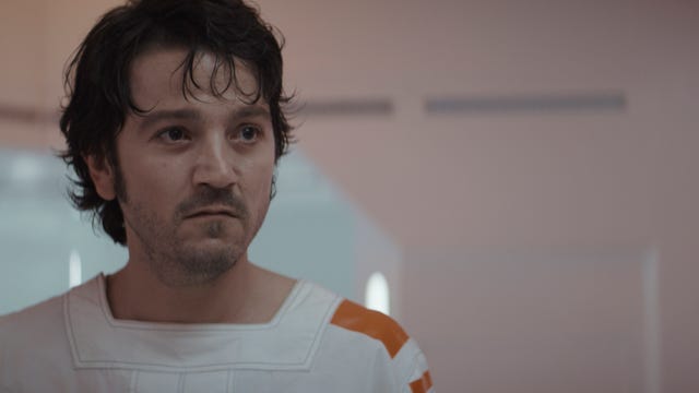 Wearing a white prison outfit, Cassian Andor looks tired but determined in Andor.
