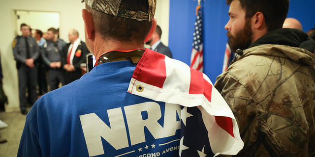 man in blue NRA shirt with US flag draped on shoulder
