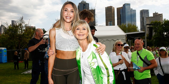 Chloe Lattanzi in a crop top and leggings holds on to her mother Olivia Newton-John in a white and green jacket at the Olivia Newton-John Wellness Walk and Research run in 2019