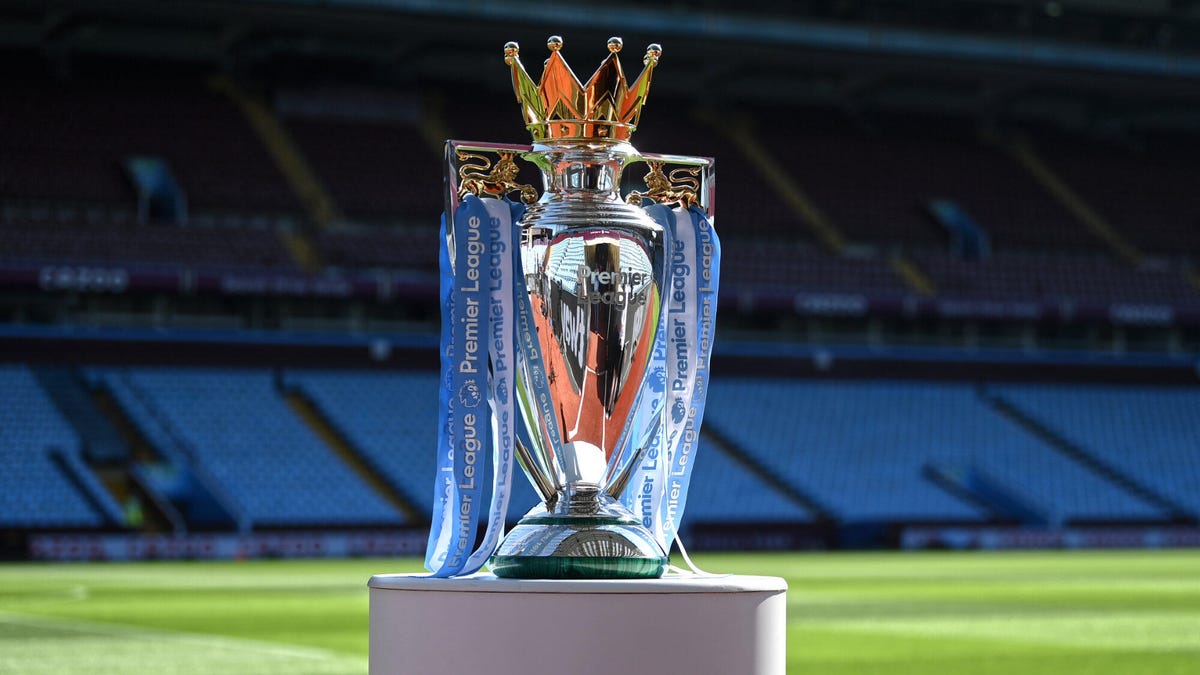 The English Premier League soccer trophy standing on a plinth in front of an empty soccer stadium stand.