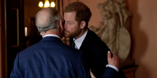 King Charles looking away as he receives a kiss on the cheek from Prince Harry