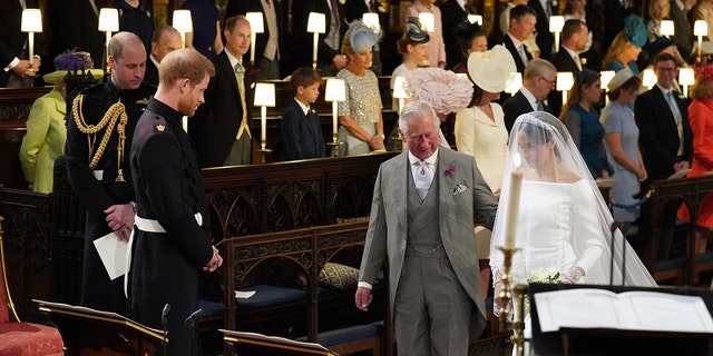 King Charles in a grey suit walking Meghan Markle in a bridal gown down the aisle