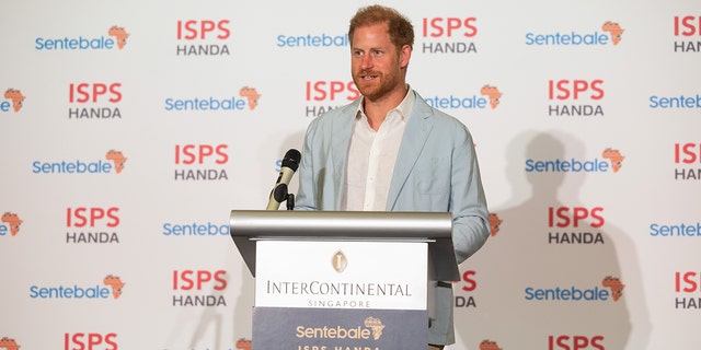 Prince Harry wearing a light blue blazer and white shirt standing in front of a podium