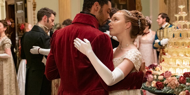 The Duke of Hastings wearing a burgundy coat dancing with Daphne Bridgerton wearing a lace white dress