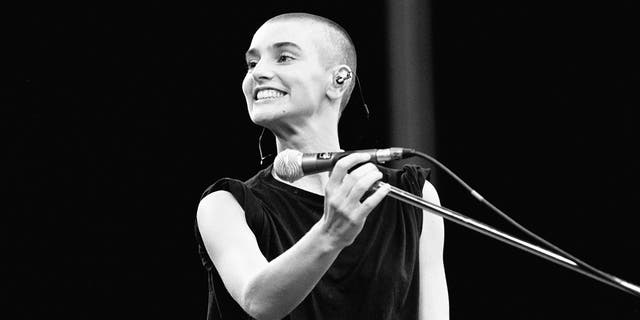 black and white photo of Sinéad O'Connor smiling at the microphone