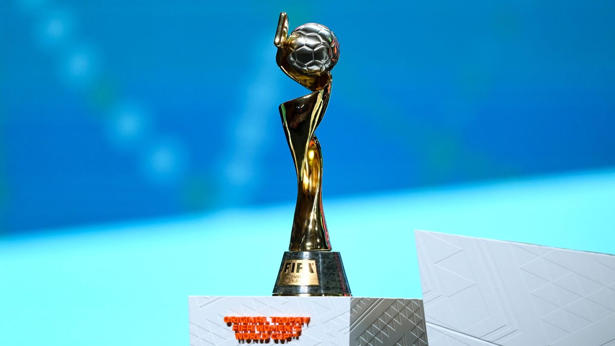 The FIFA Women's World Cup Winner's Trophy standing on a plinth in front of a blue background.