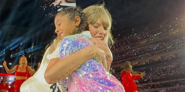 Taylor Swift in a t-shirt for her "Red" era during The Eras Tour hugs Bianka Bryant in a sparkly jacket