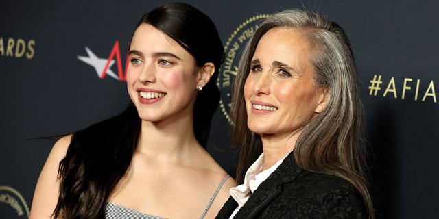 Margaret Qualley wears a grey dress on the red carpet with long dark hair next to mother Andie MacDowell in a dark suit
