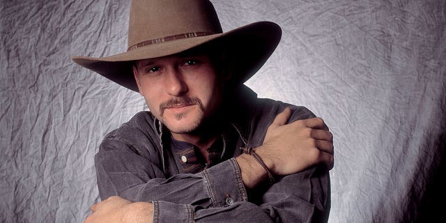 Tim McGraw poses in a cowboy hat and long-sleeve shirt