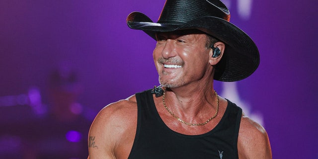 Tim McGraw performs live wearing a black tank top and matching cowboy hat
