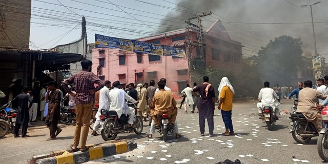 People stand on the street and watch as smoke rises from a burning church in Pakistan