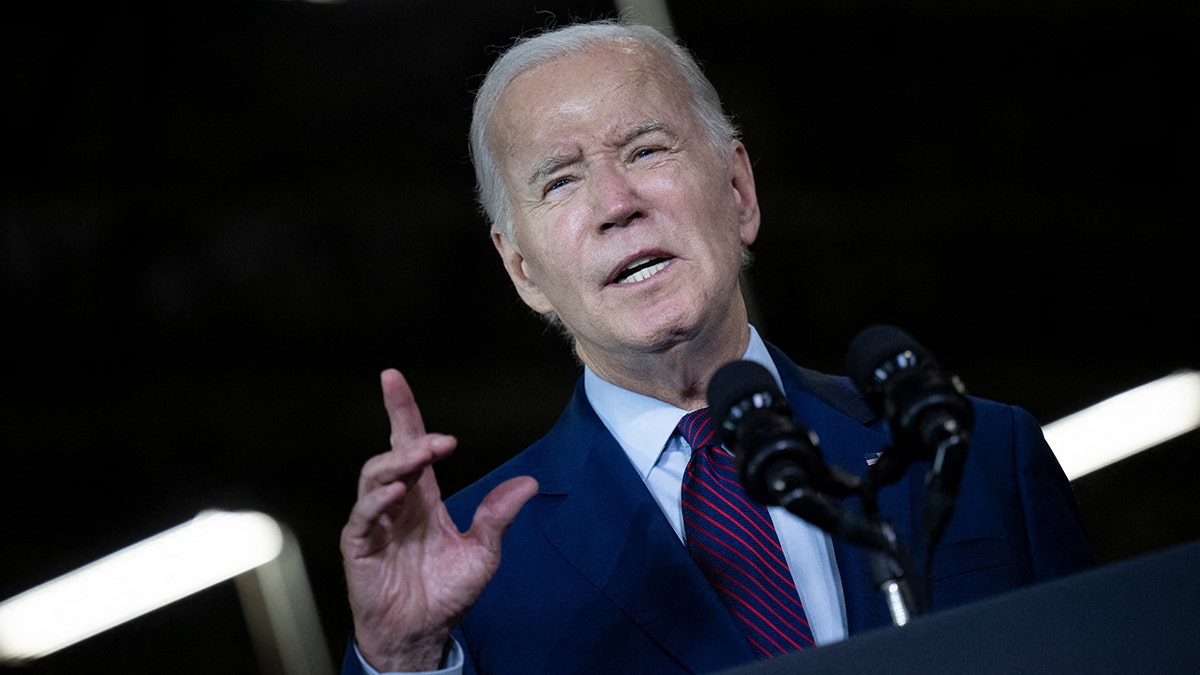 Joe Biden squinting, hand raised at podium