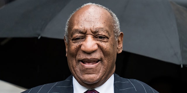 Bill Cosby smiles in a patterned suit jacket and purple tie outside the courthouse in Pennsylvania 