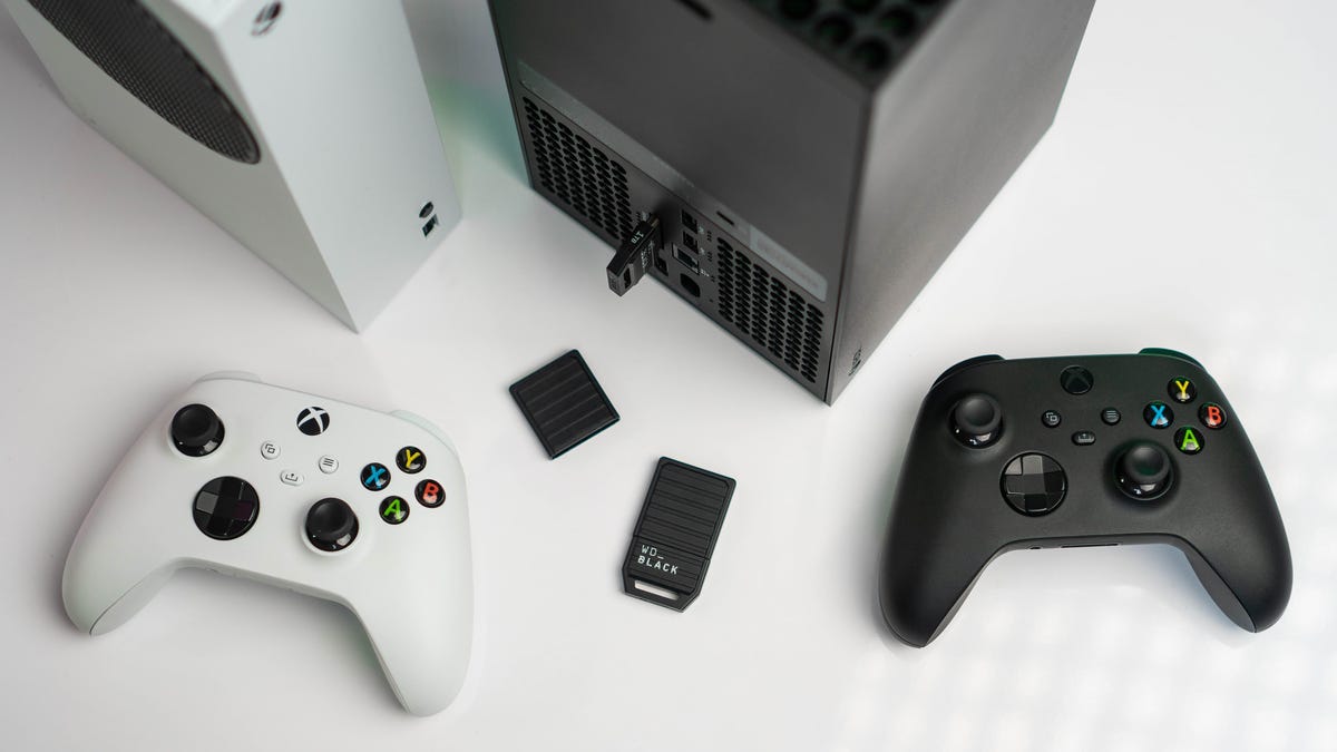 an xbox series x and s next to a white and a black xbox controller with the black c50 in the middle