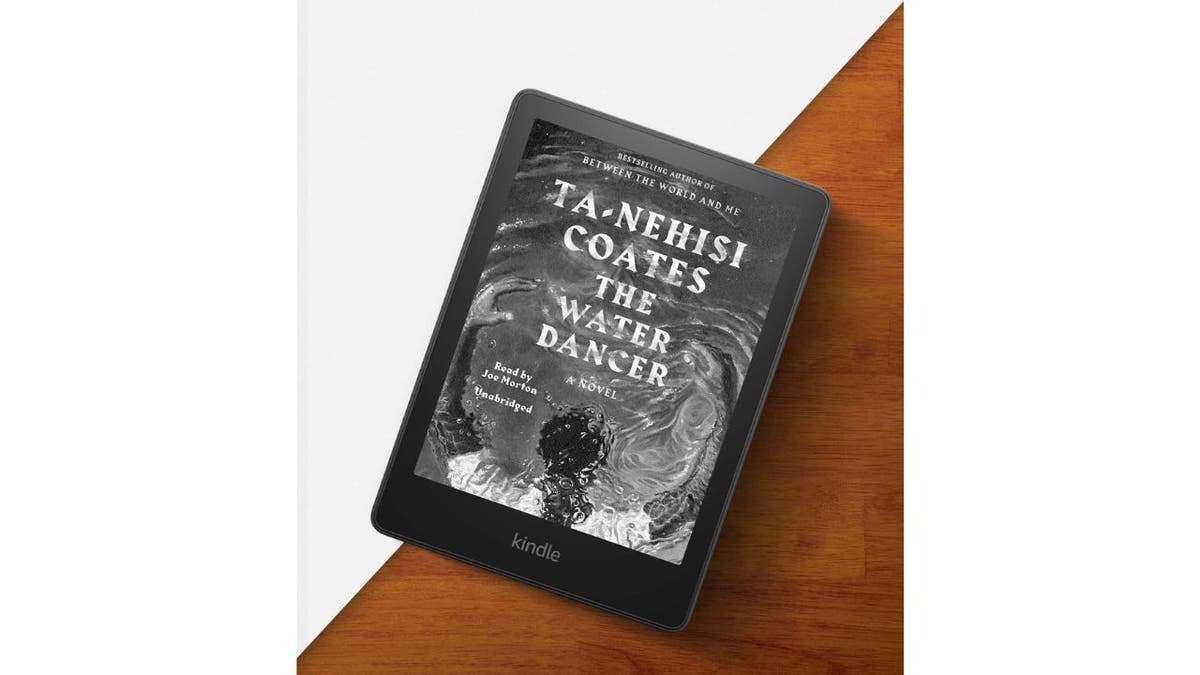 Book cover on an Amazon Kindle in black and white on a brown wooden table