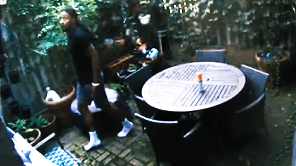 Christopher Haynes sneaks across a patio wearing black shirt, gray shorts and socks