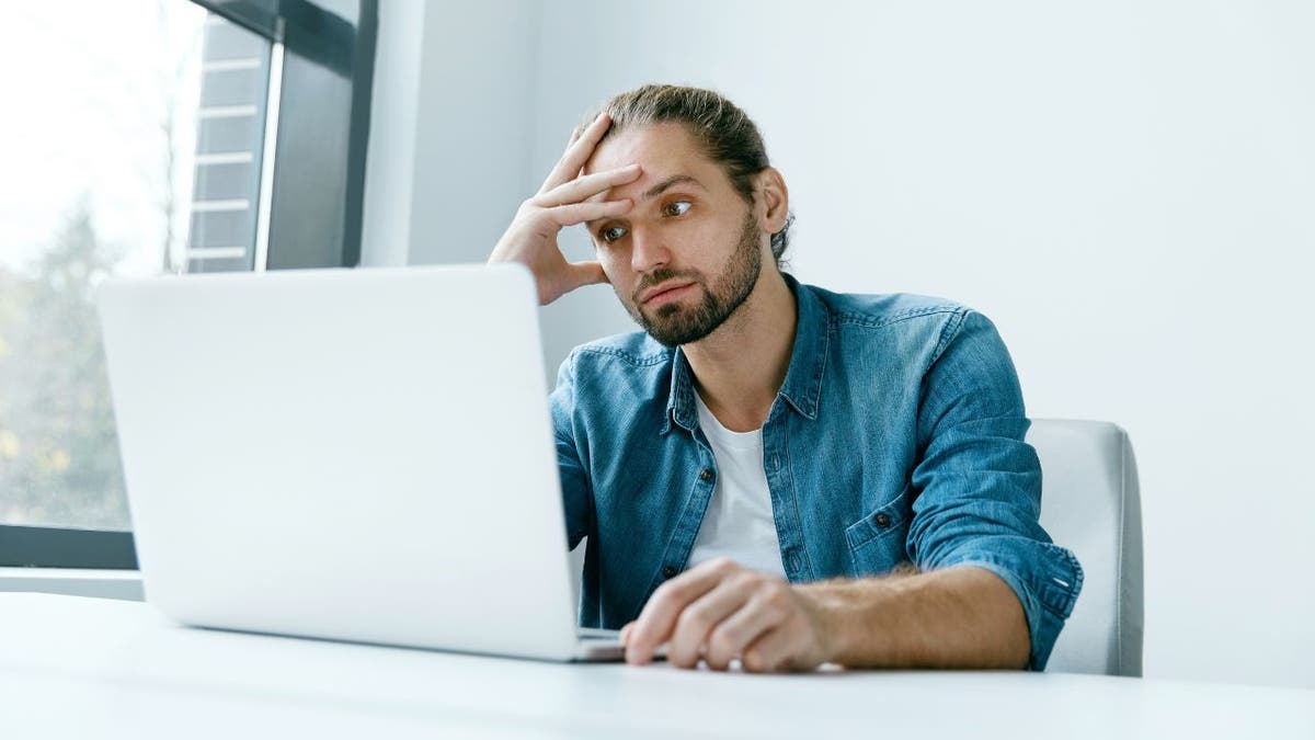 Man visibly stressed, looking at his laptop.