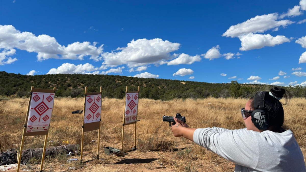 woman holds gun at outdoor New Mexico range