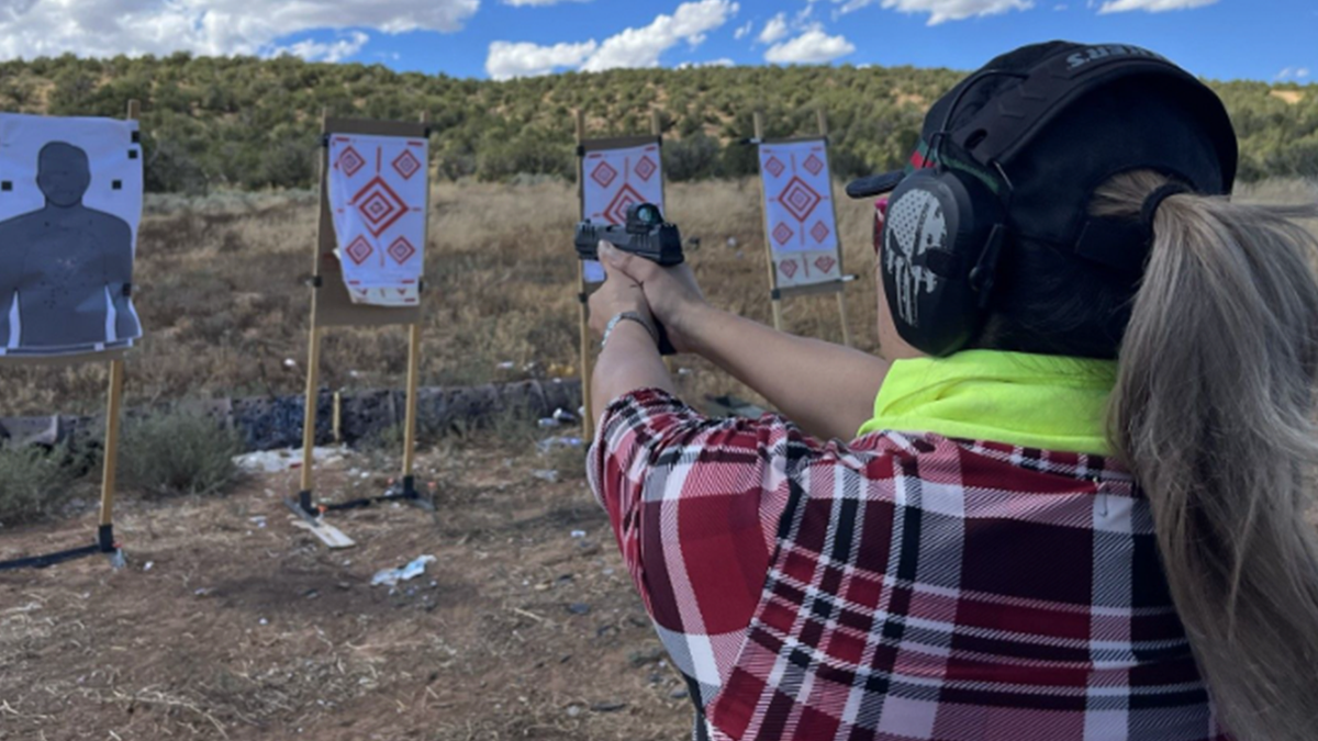 Woman holds pistol at outdoor shooting range