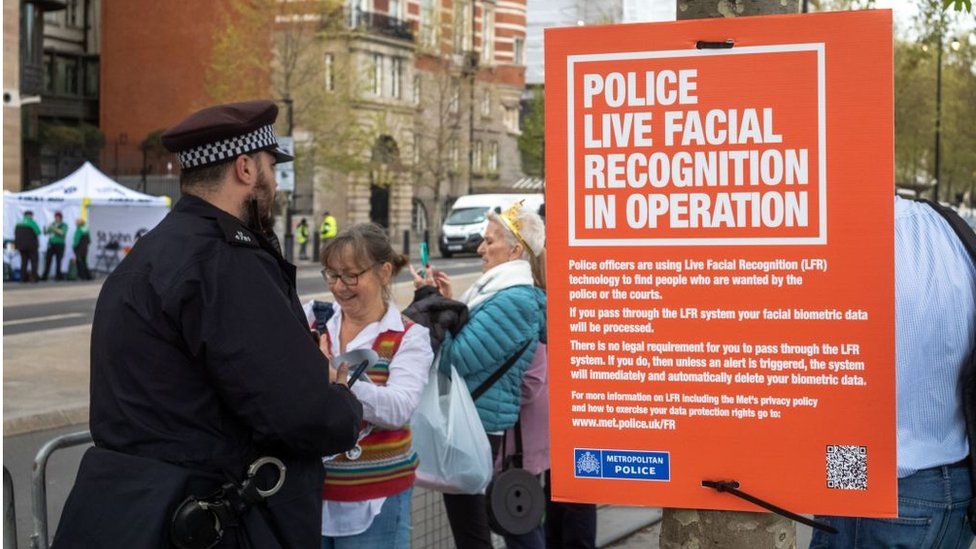 A police officer standing next to a sign which says: 'Police live facial recognition in operation'