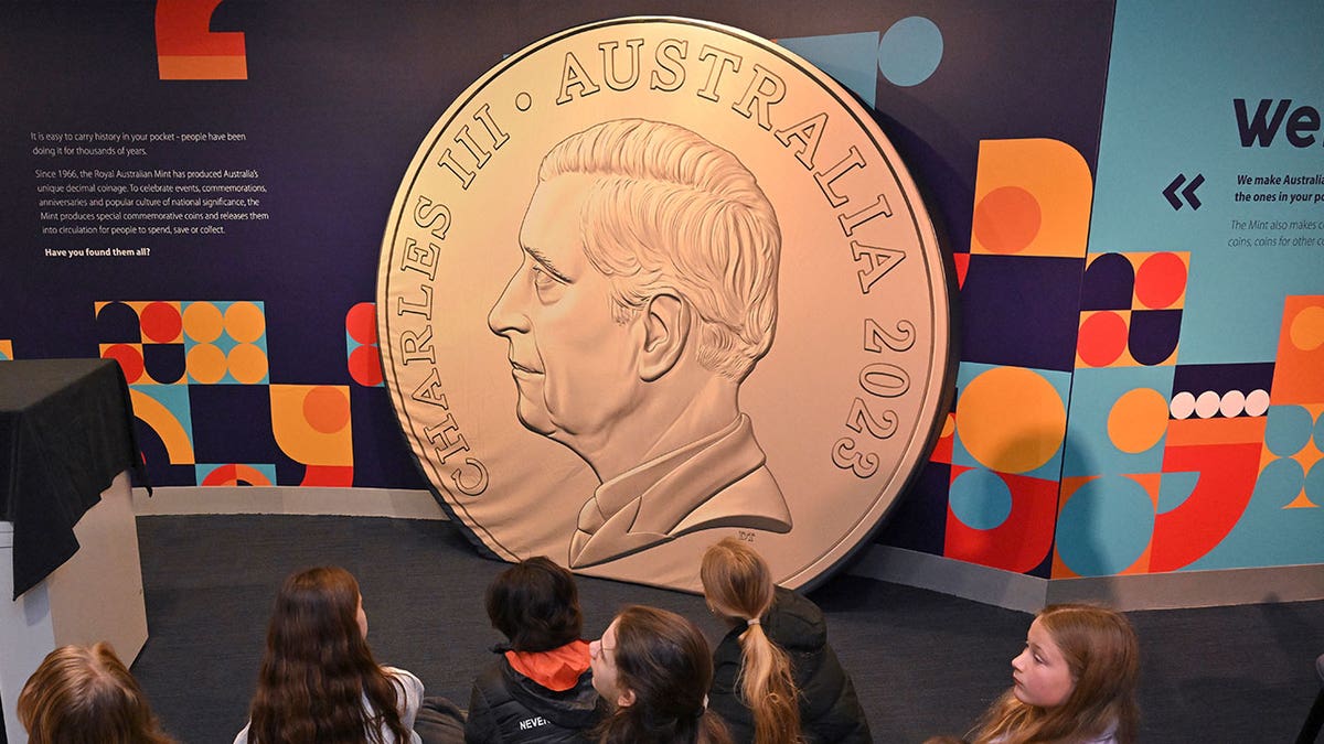 Schoolchildren look at a large mockup of a new coin 