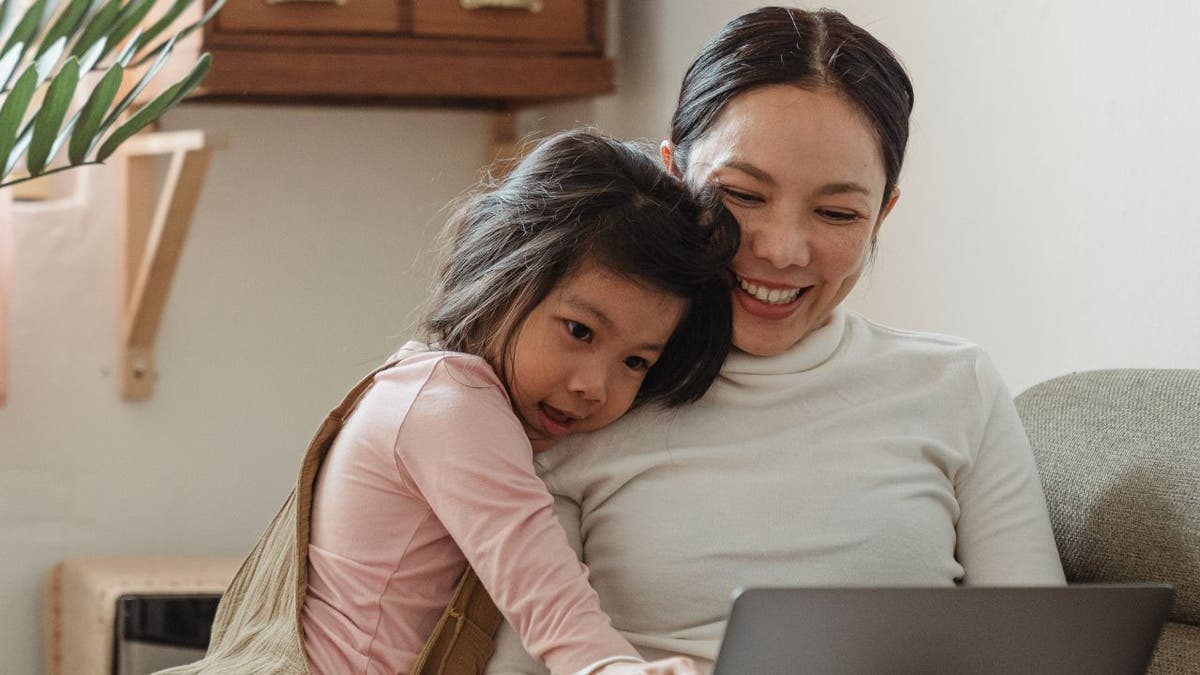 daughter hugs mother as they look at laptop