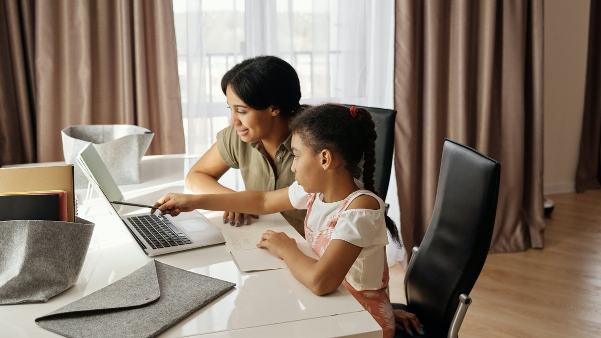 mother, daughter sit together looking at laptop