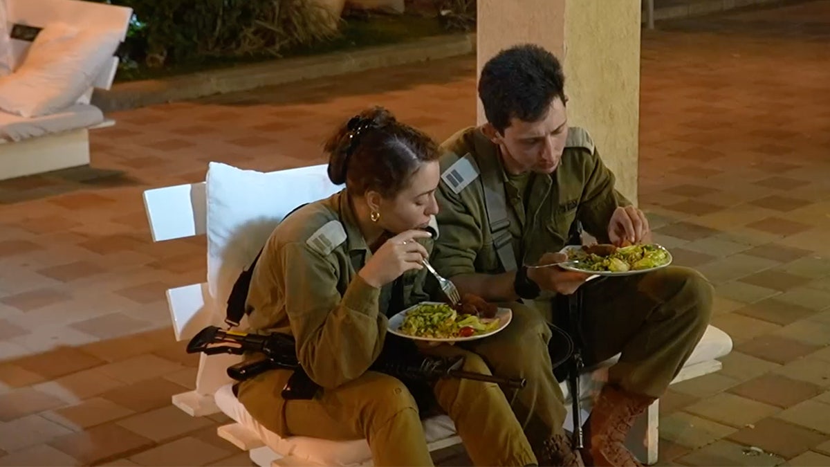 Two soldiers in green uniforms eat at a wedding.