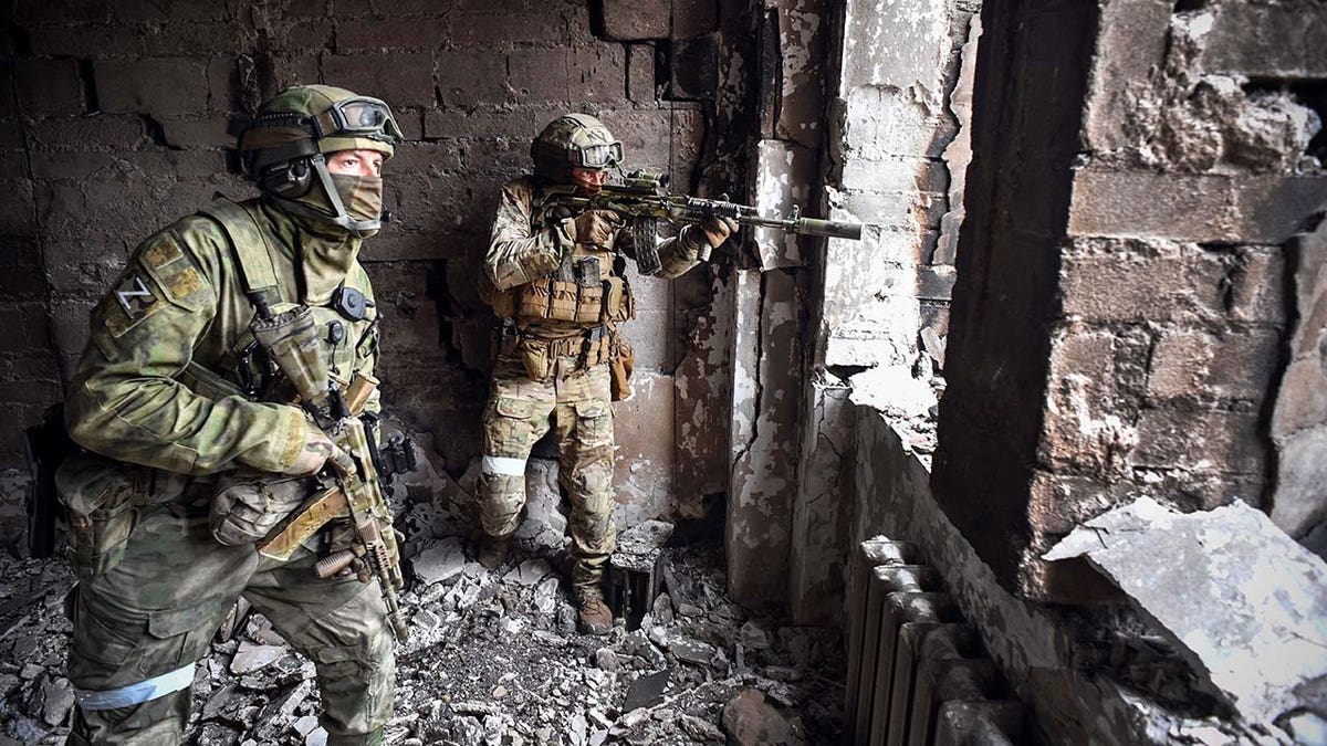 Two soldiers hold guns while patrolling war wreckage.