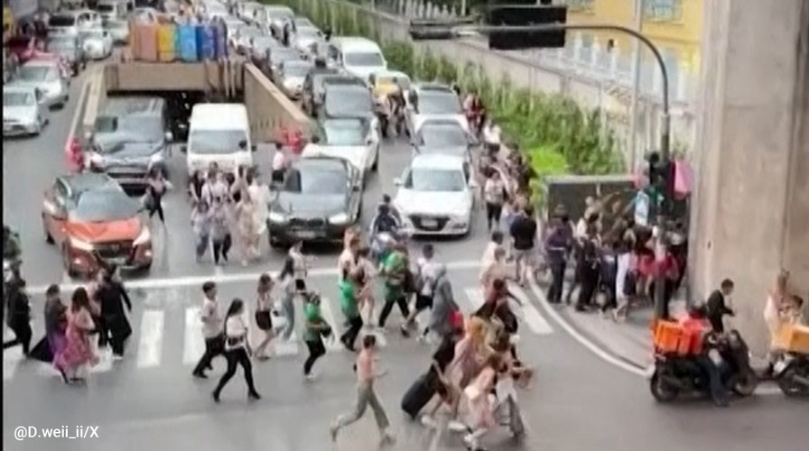 Bystanders run from a Bangkok mall after a gunman opened fire and killed three