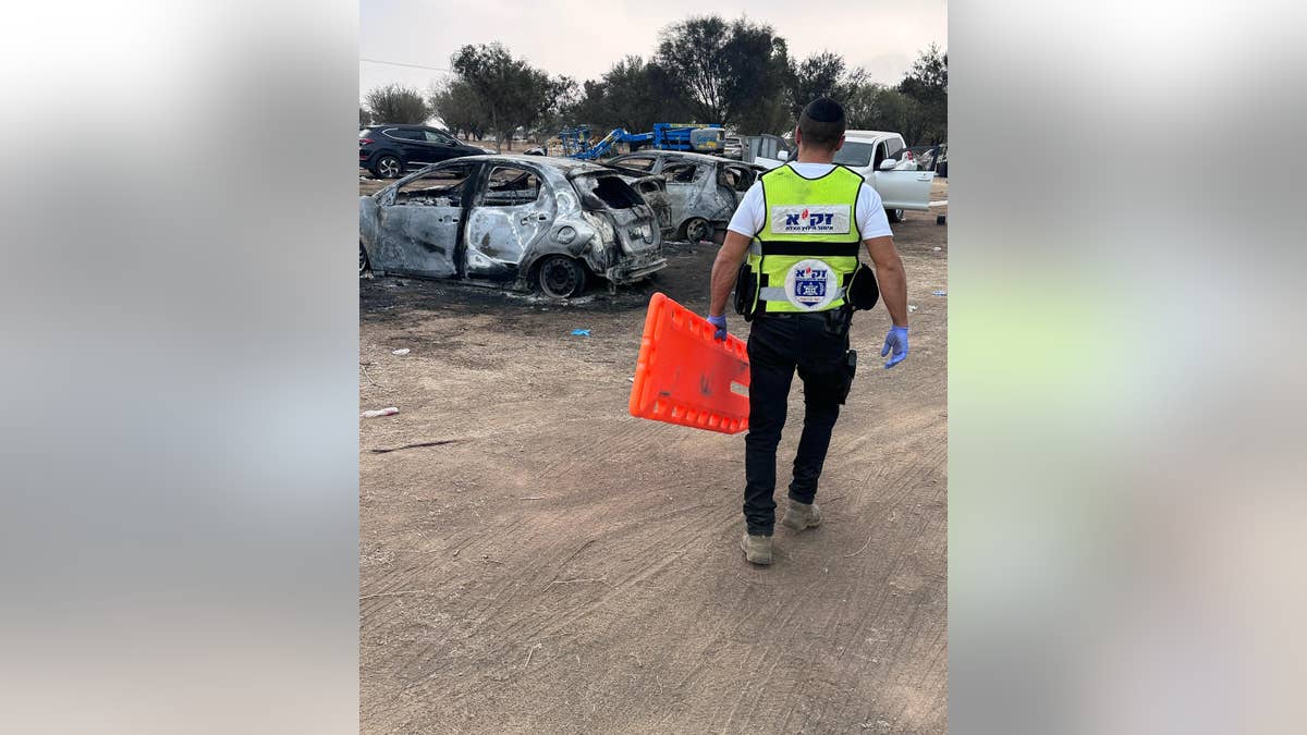 ZAKA volunteer walking with stretcher toward burned down cars