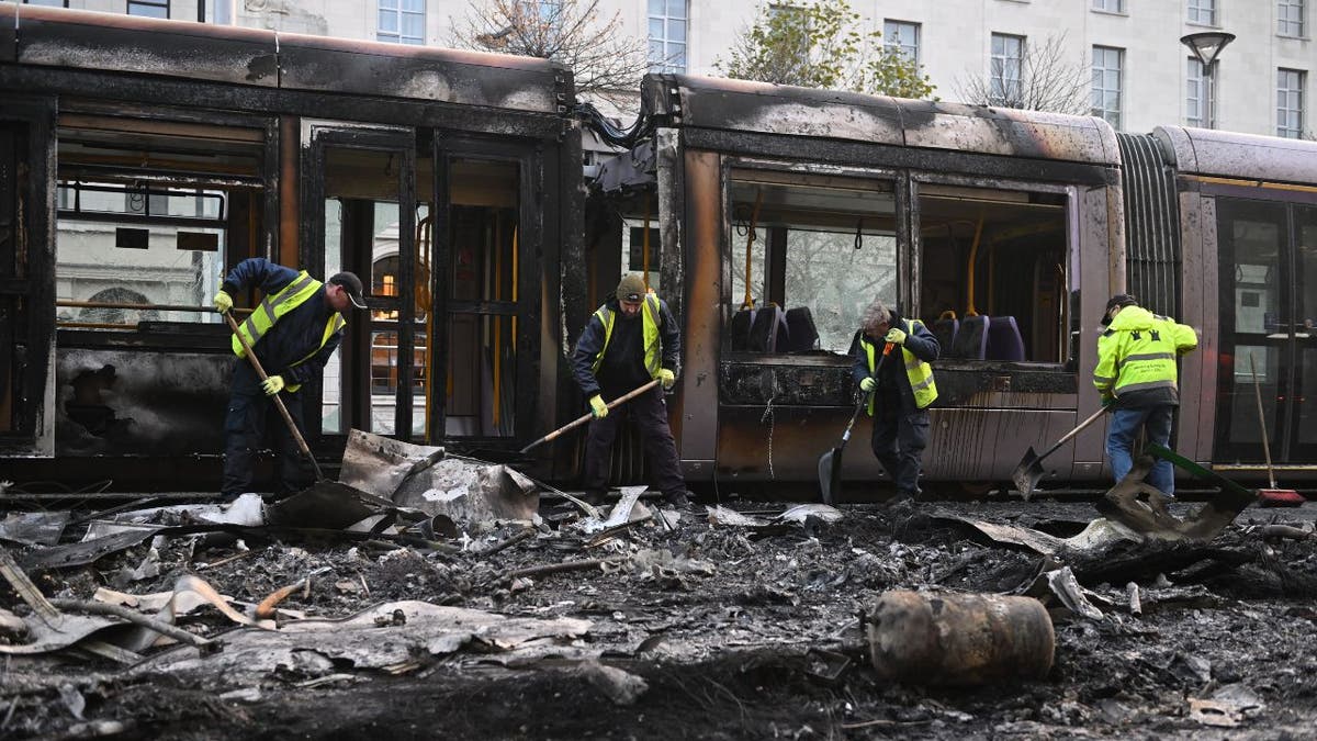 Workers clean up the debris of a burnt train in Dublin following riots