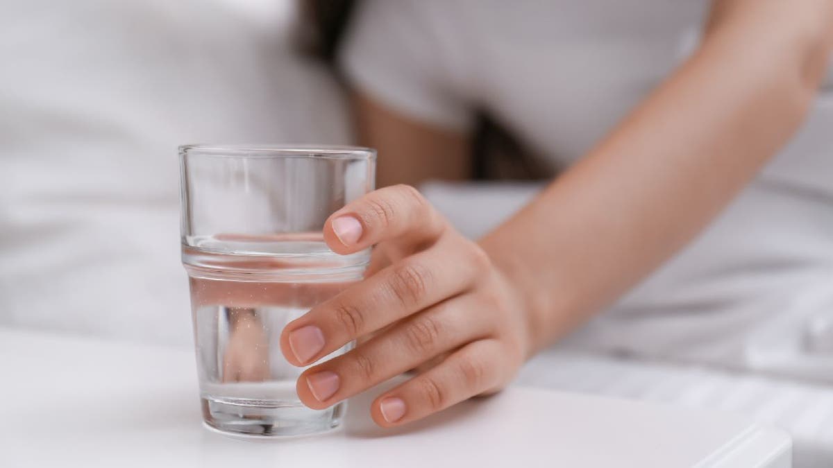 Woman reaches for water glass near bed